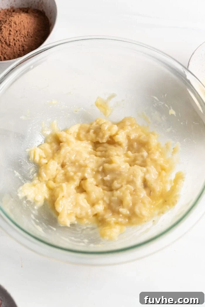 Plant-Powered Protein Brownies 4 Mashed banana in a clear glass mixing bowl, ready for the next ingredients.