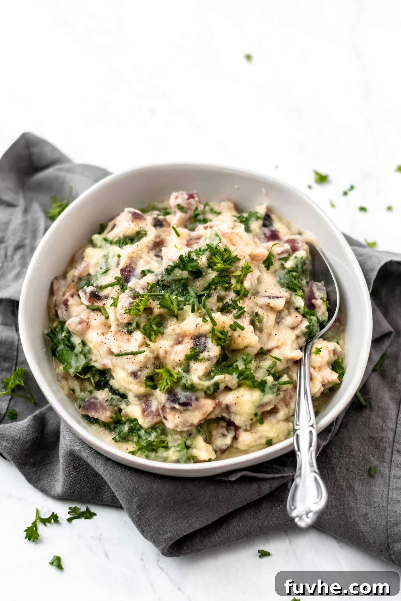 A bowl of mashed cauliflower with kale and mushrooms sitting on a grey napkin on a white surface.