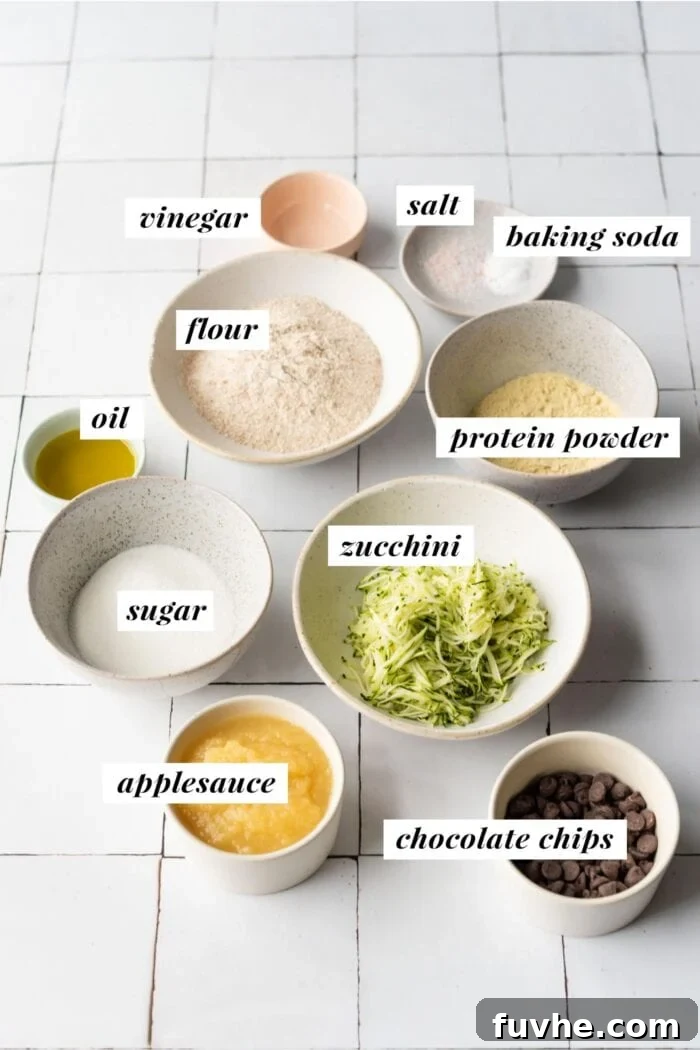 Protein-Powered Zucchini Muffins 3 Visual ingredient list for making chocolate chip zucchini protein muffins, including zucchini, flour, chocolate chips, and applesauce.