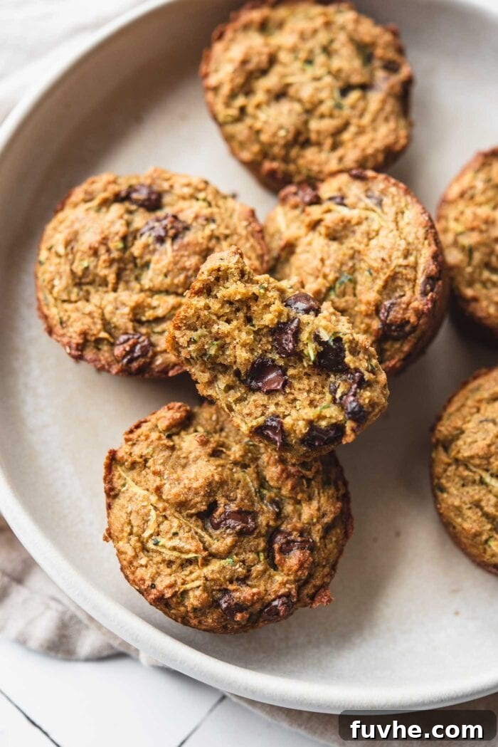 Protein-Powered Zucchini Muffins 10 Chocolate chip zucchini muffins on a plate with one cut open to show the inside texture, revealing its moist crumb and scattered chocolate chips.