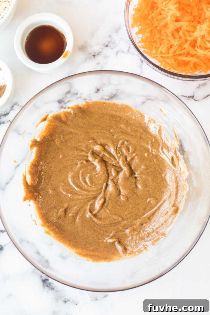 Carrot Cake Oatmeal Cookies 4 A glass mixing bowl with almond butter and brown sugar thoroughly creamed together, forming a smooth, light mixture.