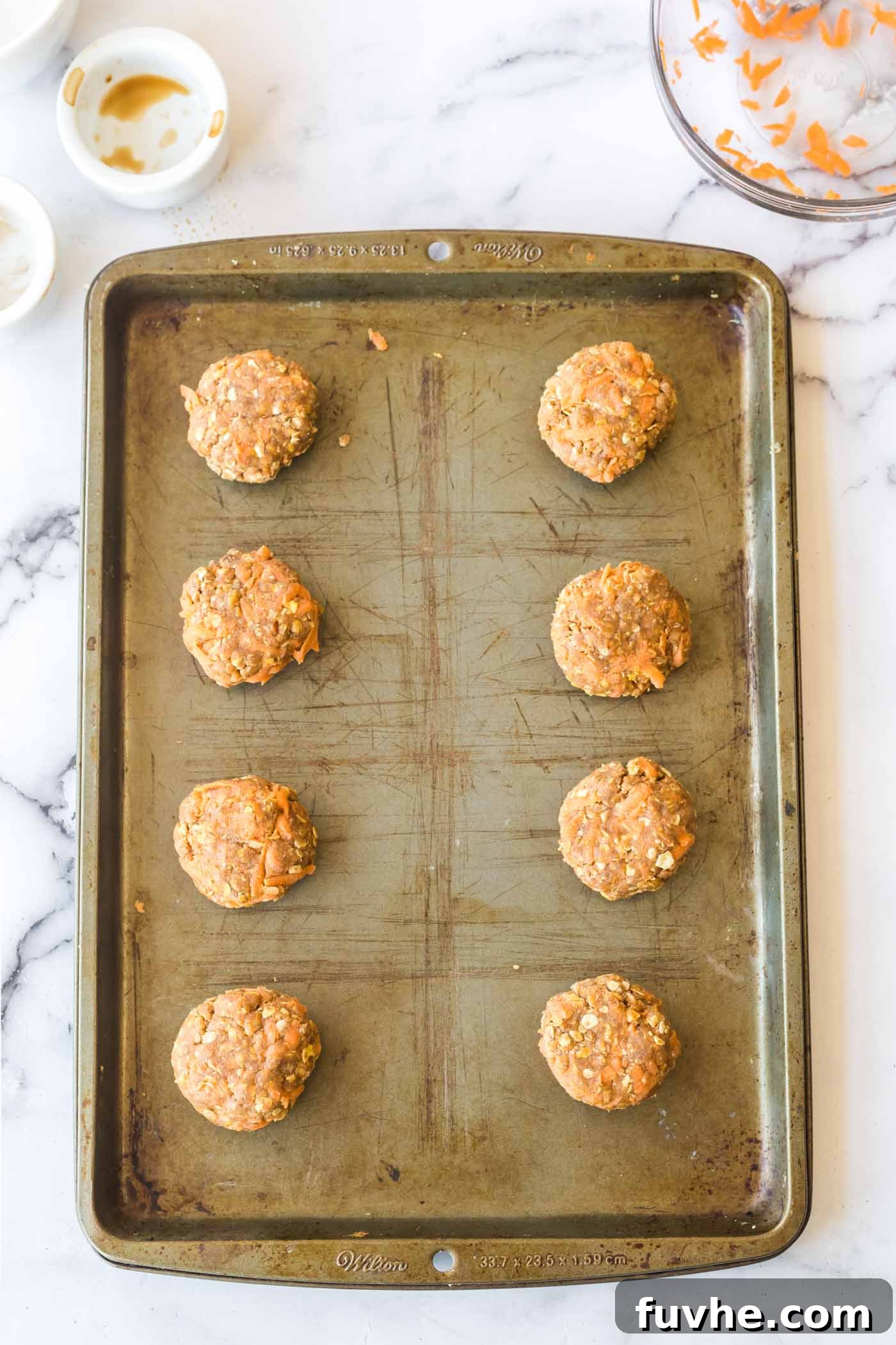 Carrot Cake Oatmeal Cookies 6 Raw cookie dough discs perfectly shaped and placed on a baking sheet, ready for the oven.