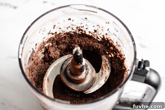 Thick, rich chocolate coconut brownie batter ready for baking, swirled beautifully within a food processor bowl.