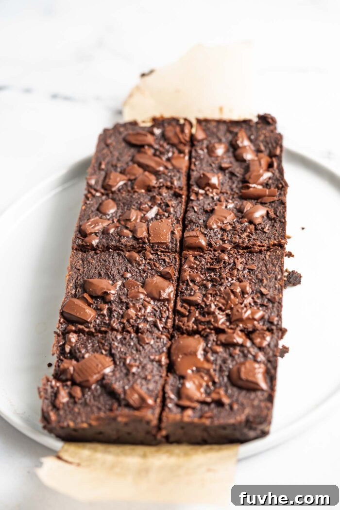 A perfectly baked slab of chocolate coconut protein brownies, freshly cut into eight portions, resting on a sheet of parchment paper on a serving plate.