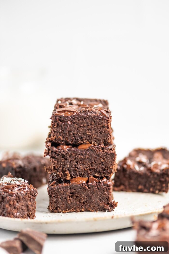 A tempting stack of three fudgy vegan chocolate coconut protein brownies, adorned with a drizzle of melted chocolate, served on an elegant plate.