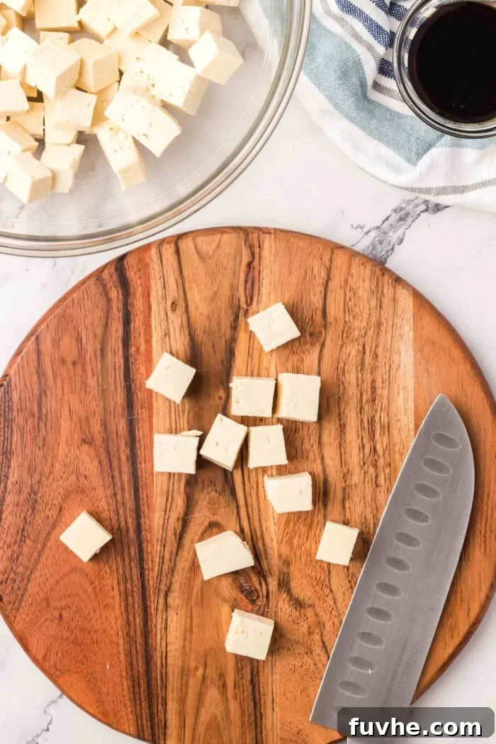 A number of firm tofu cubes neatly arranged on a bamboo cutting board, with a chef's knife resting beside them, ready for seasoning.