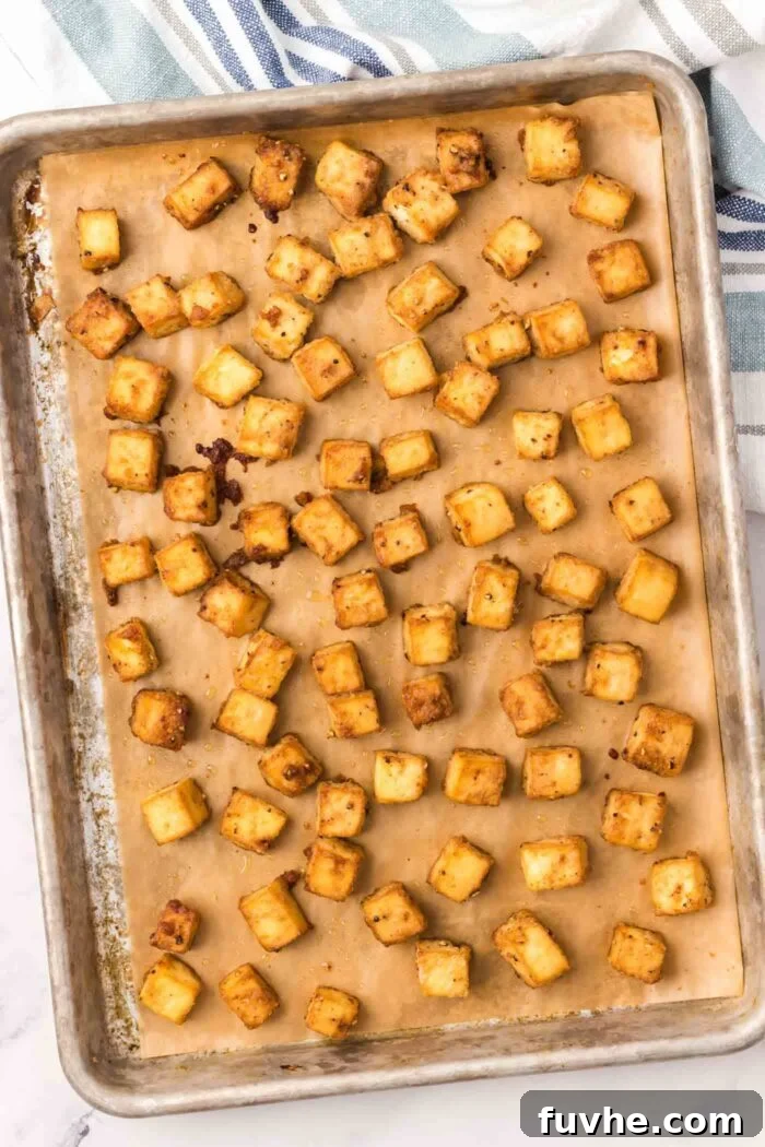 Crispy baked tofu cubes uniformly spread on a baking sheet lined with parchment paper, fresh out of the oven and golden brown.