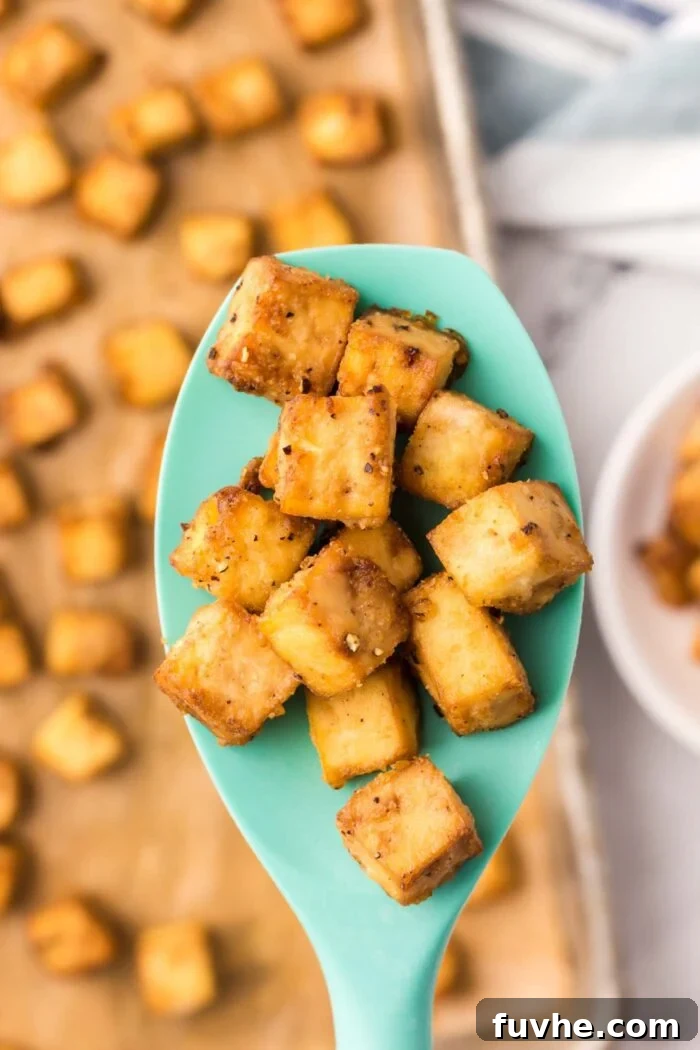 Several cubes of crispy baked tofu resting on a gray silicone serving spoon, showing their textured and golden surface.