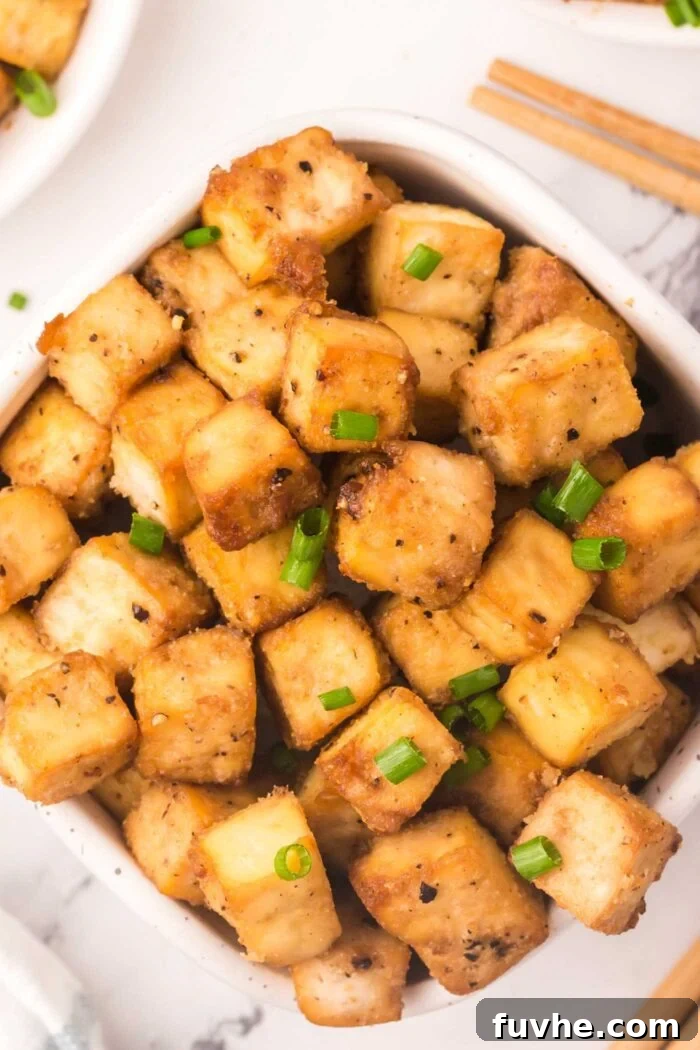 A large rustic bowl filled with numerous crispy baked tofu cubes, generously garnished with fresh green onion slices, ready to be served.