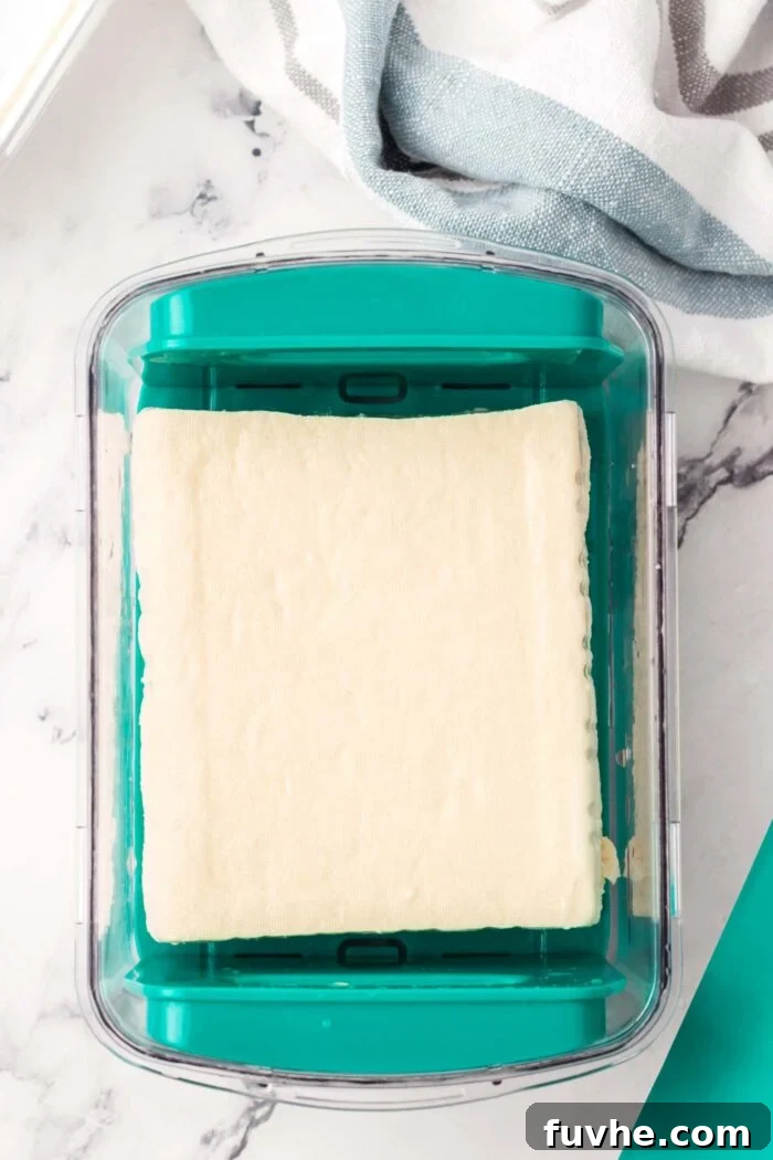 A block of firm tofu visibly pressing in a dedicated tofu press, extracting excess water for optimal scramble texture.