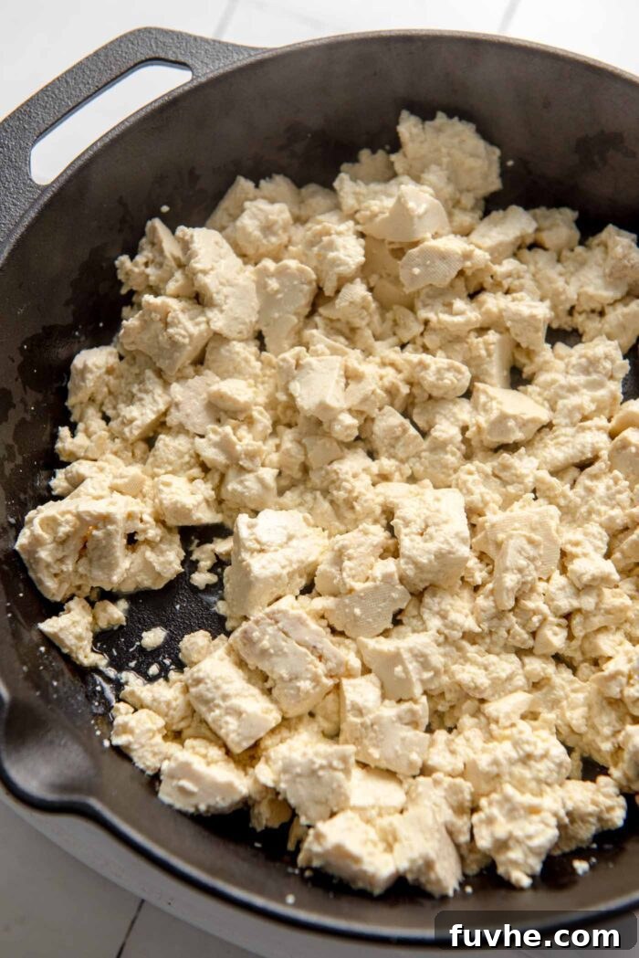 Perfectly crumbled tofu bits sizzling and browning in a hot cast iron skillet, taking on a golden hue.