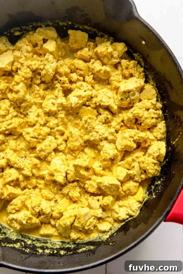 The golden tofu scramble, rich with turmeric and spices, actively cooking and absorbing its creamy sauce in a cast iron skillet.