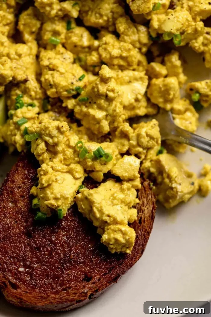 Delicious bits of golden tofu scramble generously piled on a piece of rustic toast, elegantly presented in a bowl for a cozy and satisfying breakfast.