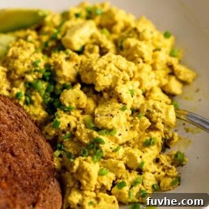 Tofu scramble topped with chopped chives in a bowl with a piece of toast.