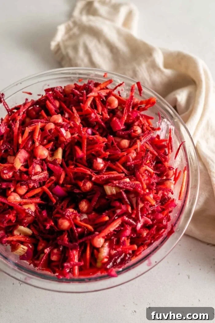 A large glass mixing bowl filled with a freshly prepared beet and chickpea salad, perfectly tossed with its creamy dressing and ready to be served.