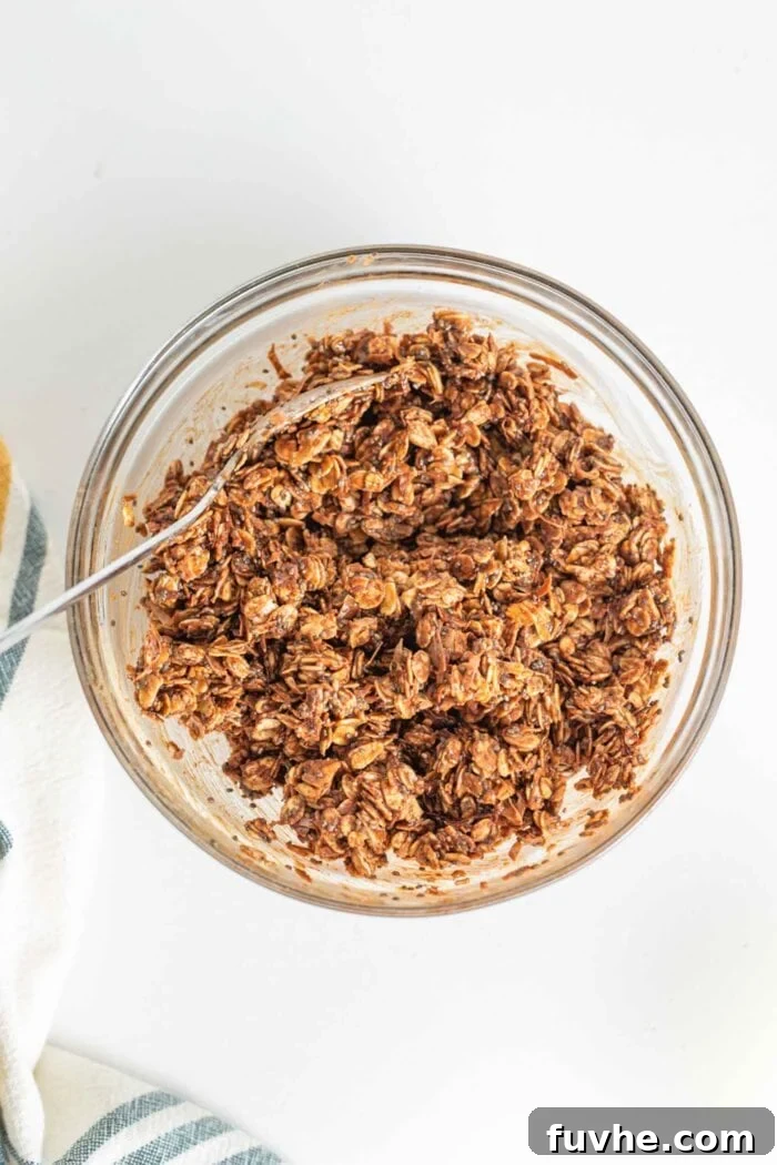A delightful crumbly chocolate oat mixture, studded with chia seeds, resting in a clear glass mixing bowl, awaiting transfer to the pan.