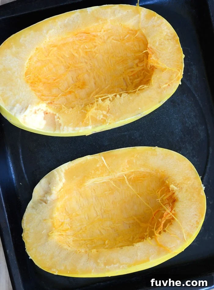Cut spaghetti squash halves placed face up on a baking tray, ready for seasoning and roasting.