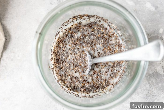 Raw chia seeds being added to almond milk in a glass jar.