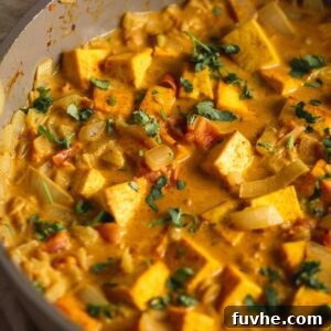 A creamy coconut curried tofu with diced tomato and onion topped with fresh cilantro cooking in a skillet.