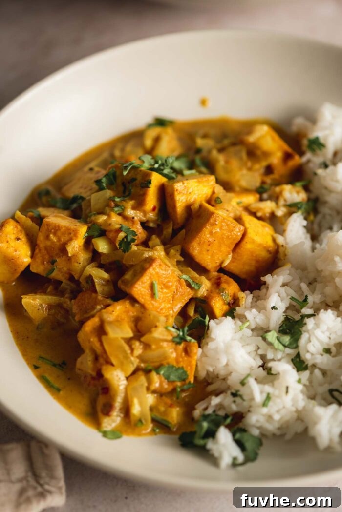 Curried tofu served in a bowl with rice topped with a sprinkle of fresh cilantro.