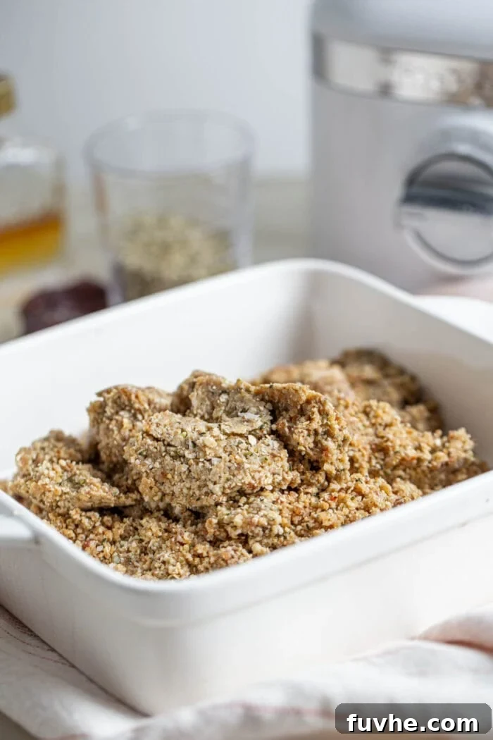 Crumbly but cohesive tahini hemp seed bar dough in a square baking dish, ready for pressing.