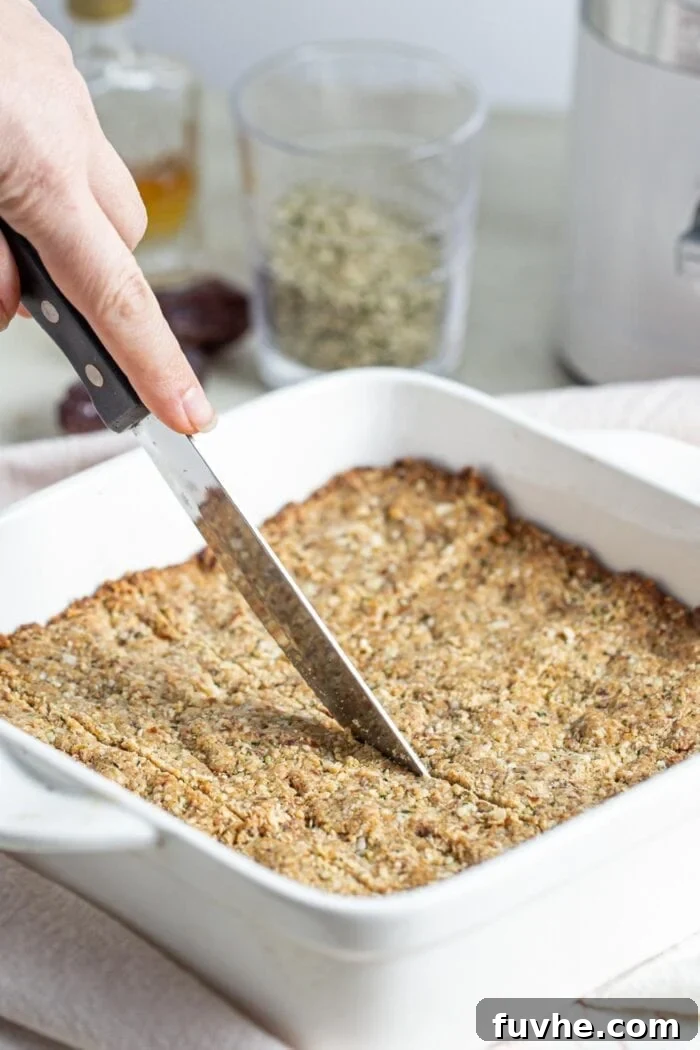 A knife cutting into freshly baked tahini hemp seed bars directly in the baking dish, revealing their soft interior.