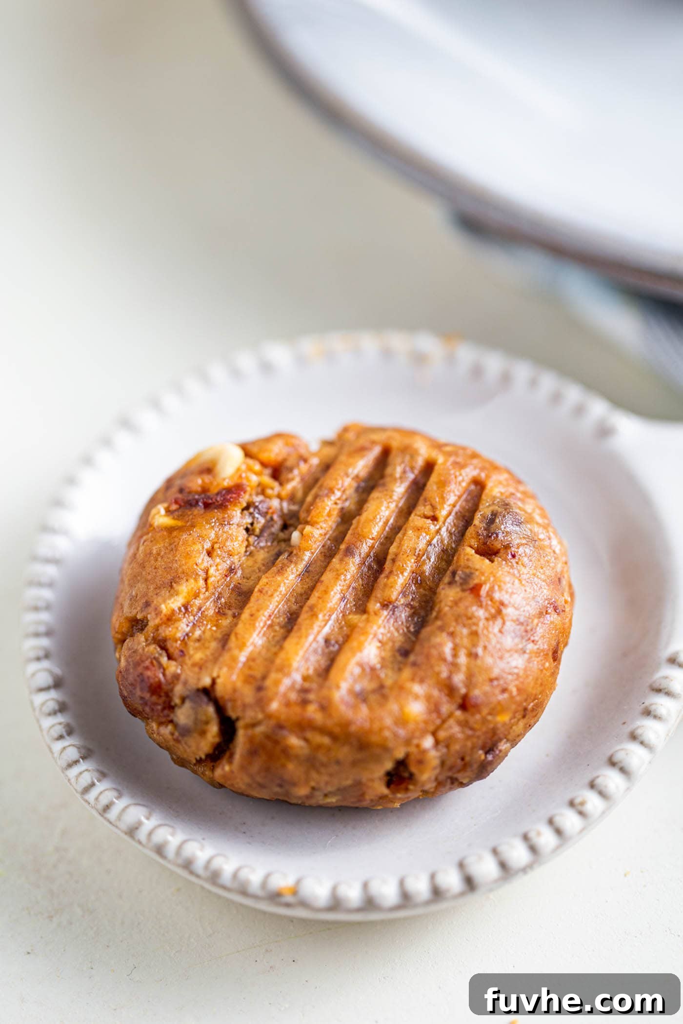 A perfectly shaped no-bake peanut butter chocolate chip cookie, garnished with a few chocolate chips, resting on a small white plate.