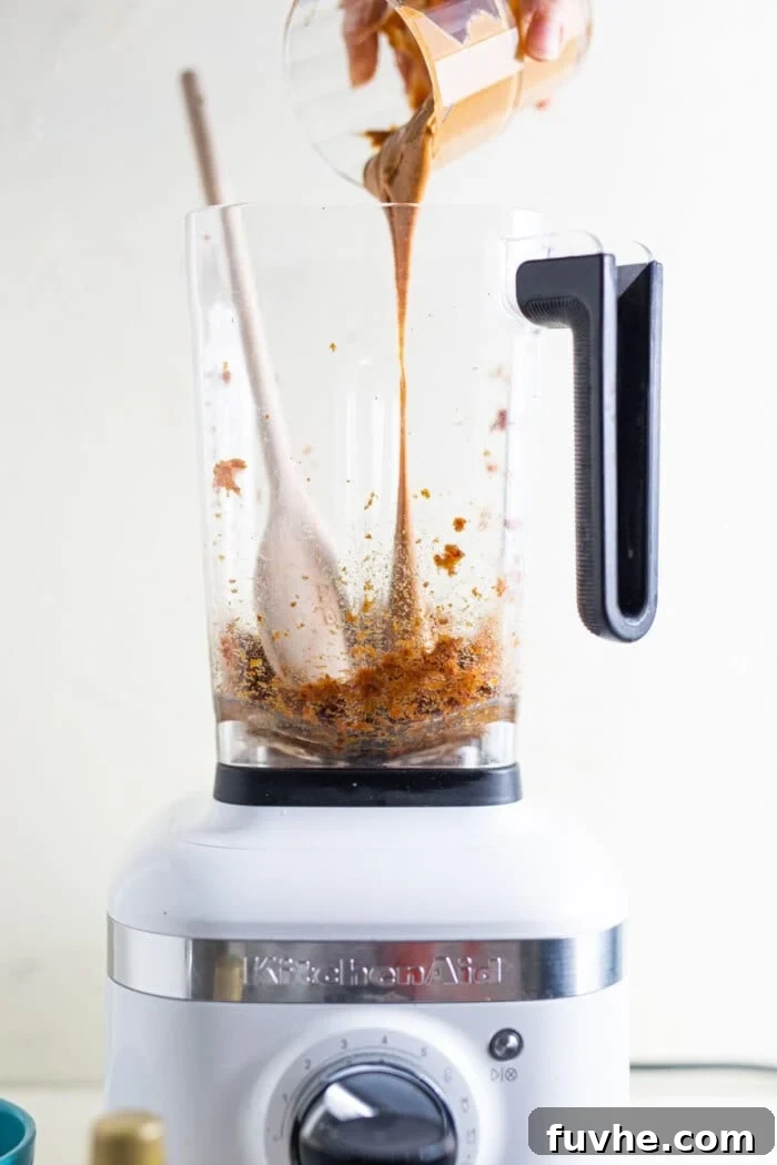 Natural almond butter being poured into a food processor containing softened, blended dates.