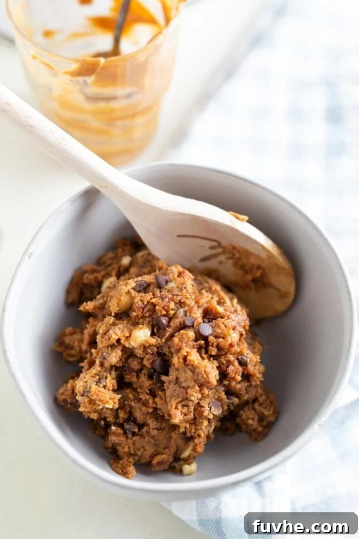 Rich, raw chocolate chip cookie dough resting in a small, clean white bowl, flecked with chocolate pieces.