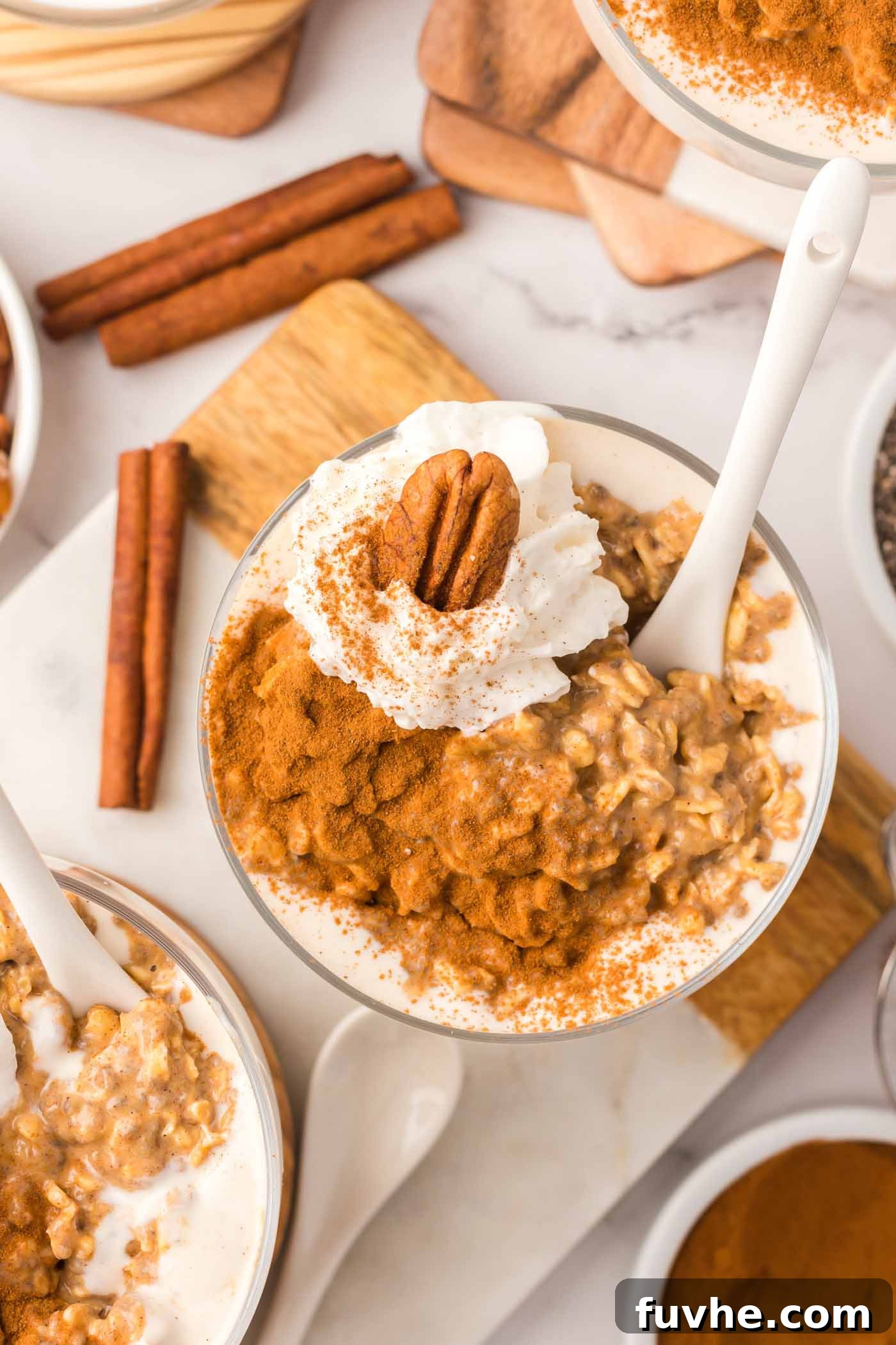 Spiced Pumpkin Overnight Oats 2 Overhead view of a parfait glass of pumpkin overnight oats topped with whipped cream, a pecan, and cinnamon.