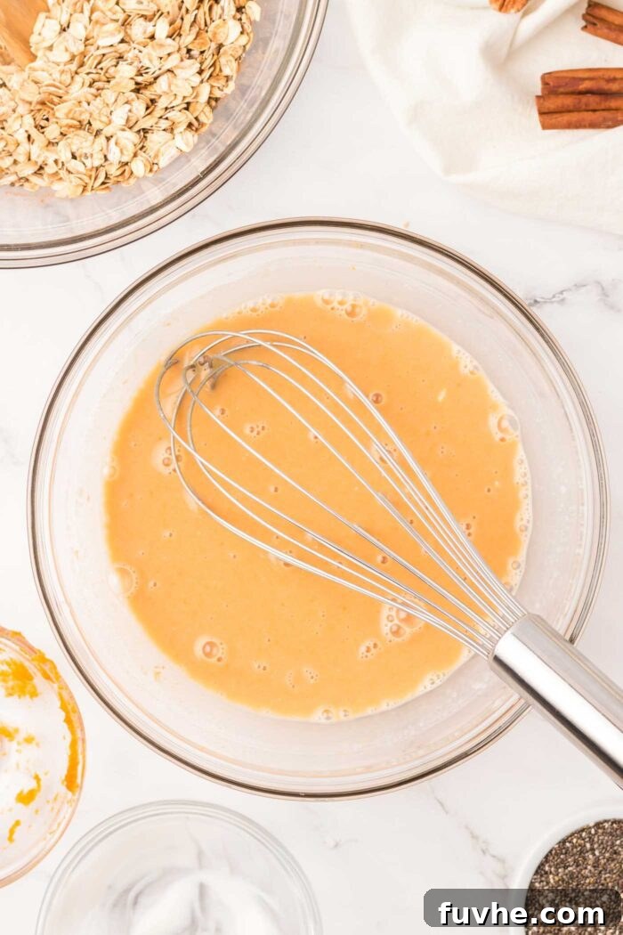 Spiced Pumpkin Overnight Oats 4 Milk with pumpkin puree mixed into it in a glass mixing bowl with a whisk in it.