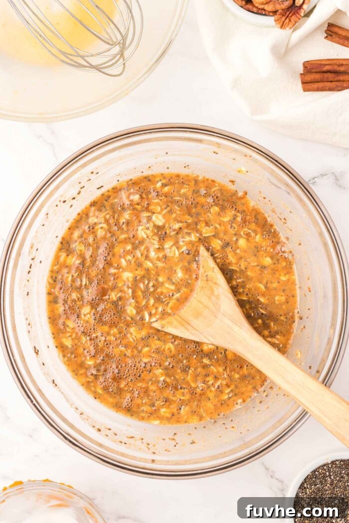 Spiced Pumpkin Overnight Oats 5 Rolled oats mixed with chia seeds, pumpkin, milk and spices in a glass mixing bowl with wooden spoon.