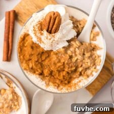 Overhead view of a parfait glass of pumpkin overnight oats topped with whipped cream, a pecan, and cinnamon.