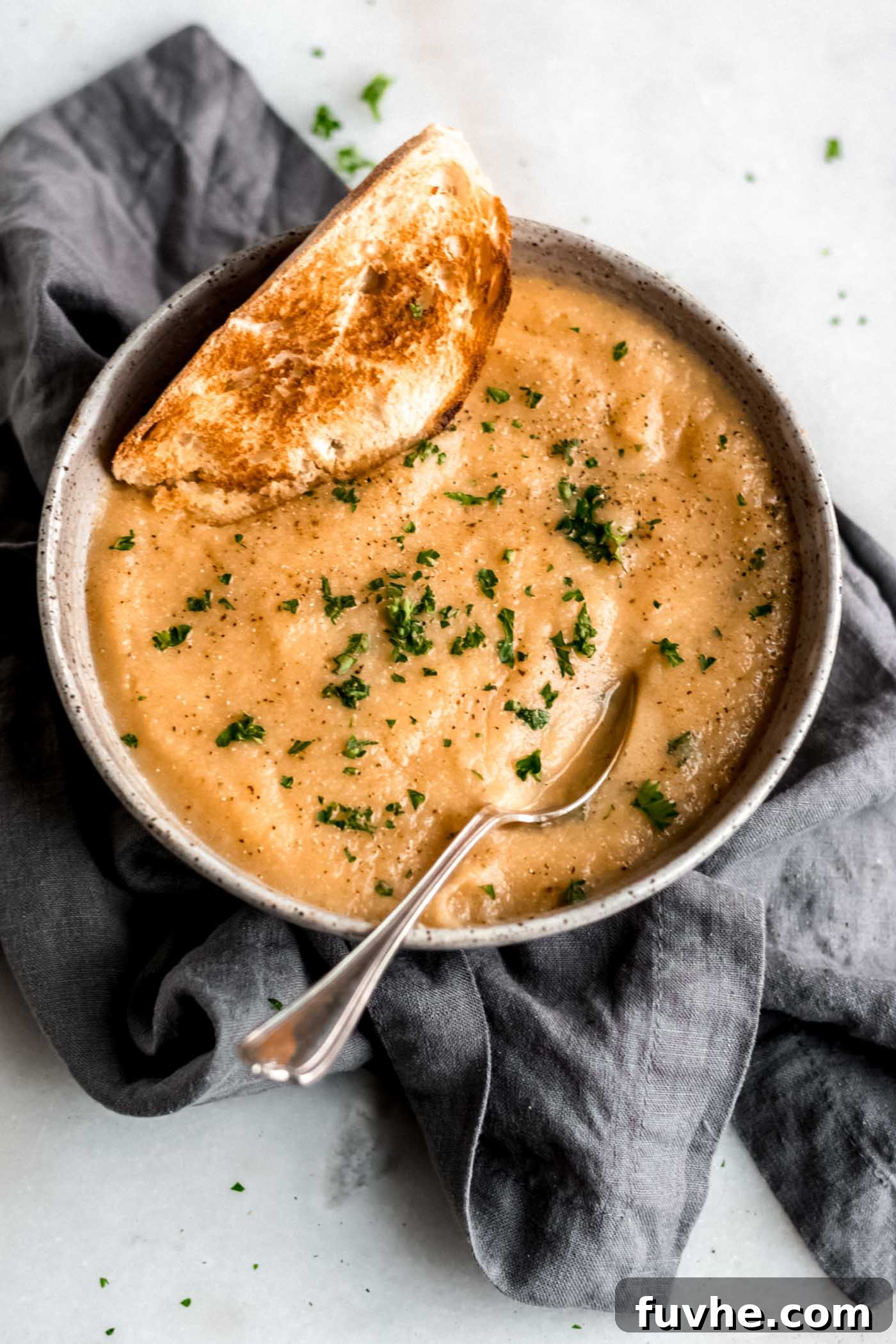 Golden Roasted Garlic Cauliflower Soup 2 Healthy vegan roasted garlic cauliflower soup with fresh toasted bread on a rustic wooden table.