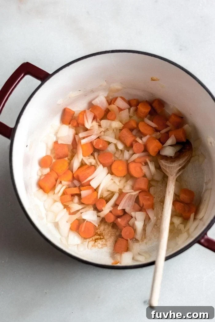 Golden Roasted Garlic Cauliflower Soup 5 Carrots and onion being stirred in a soup pot with a wooden spoon, releasing their flavors.