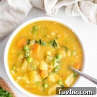 Bowl of cauliflower potato soup with peas on a white background with a beige napkin.