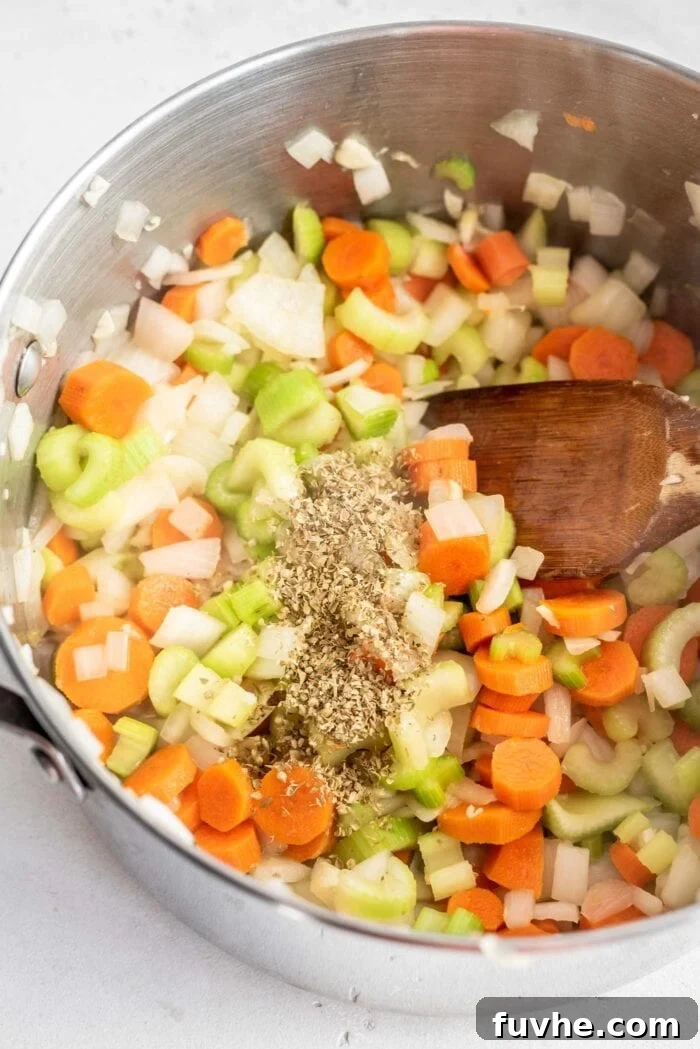 Velvety Cauliflower Potato Comfort 5 The aromatic base of onions, carrots, celery, and garlic, now infused with dried herbs like thyme and parsley, continues to cook in a soup pot, stirred by a wooden spoon.