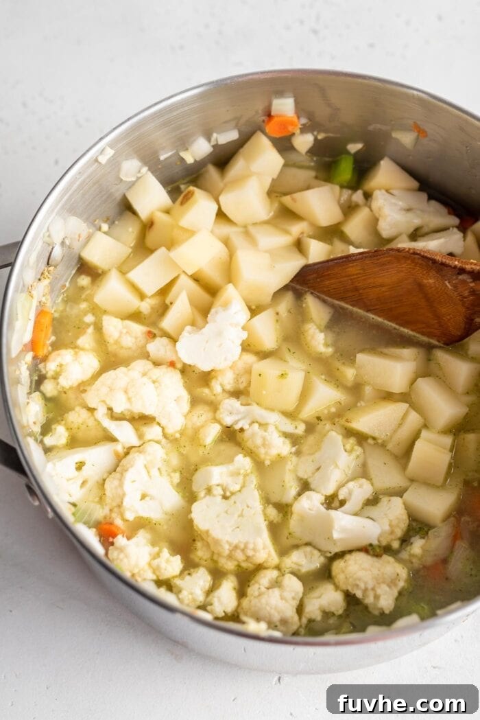 Velvety Cauliflower Potato Comfort 6 A soup pot filled with chopped cauliflower and cubed potatoes, simmering in flavorful vegetable broth alongside the sautéed aromatic vegetables.