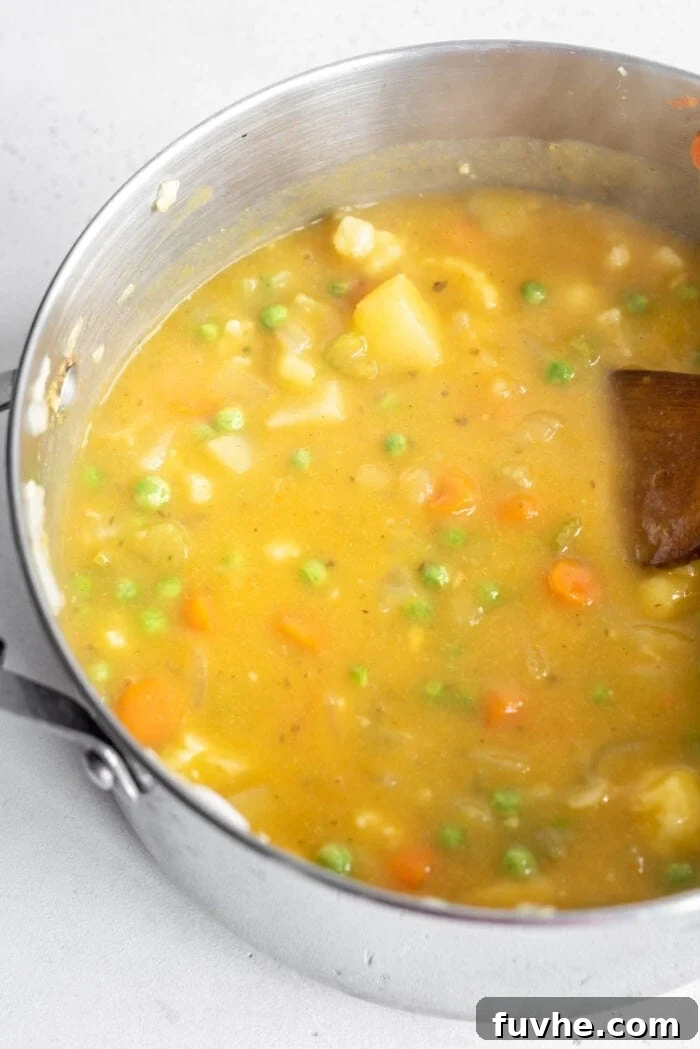Velvety Cauliflower Potato Comfort 8 A large pot filled with a vibrant, creamy cauliflower potato and carrot soup, speckled with bright green peas, with a wooden spoon resting in the pot, ready to serve.