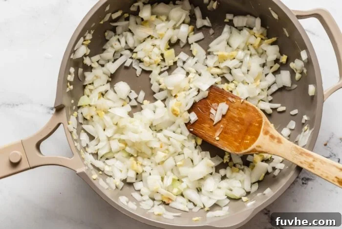 Spiced Kabocha Delight 6 Diced onion, minced garlic, and fresh ginger gently sautéing in a pan on a stovetop, being stirred with a wooden spoon, releasing their fragrant aromas.