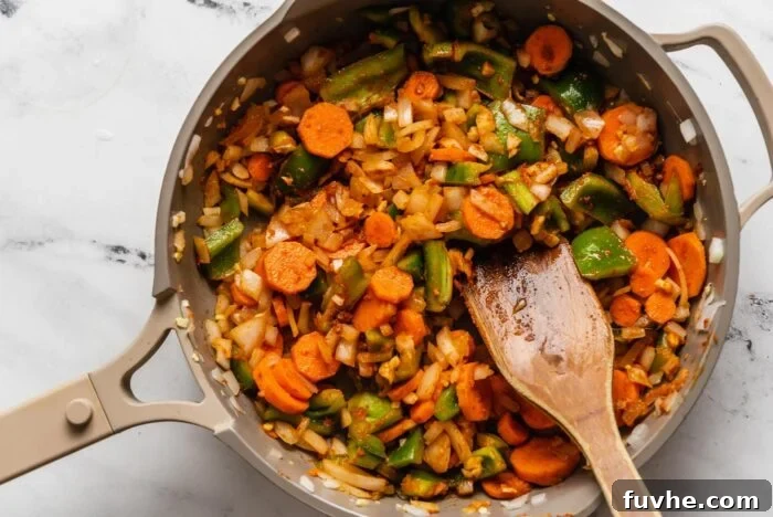 Spiced Kabocha Delight 7 Freshly chopped carrots and bell peppers mixed with onion and red curry paste, actively cooking in a skillet on the stove, infusing the ingredients with flavor.