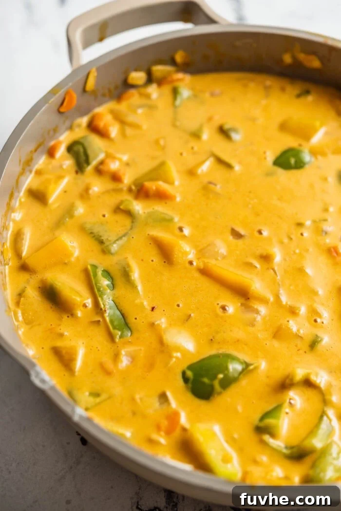 Spiced Kabocha Delight 8 A creamy red curry, rich with tender kabocha squash and colorful vegetables, simmering gently in a large skillet, ready to be served.