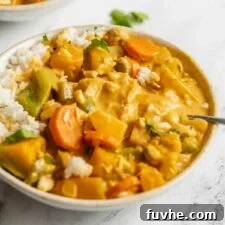 A comforting bowl of kabocha squash and vegetable red curry served over rice, with a spoon resting invitingly in the bowl.