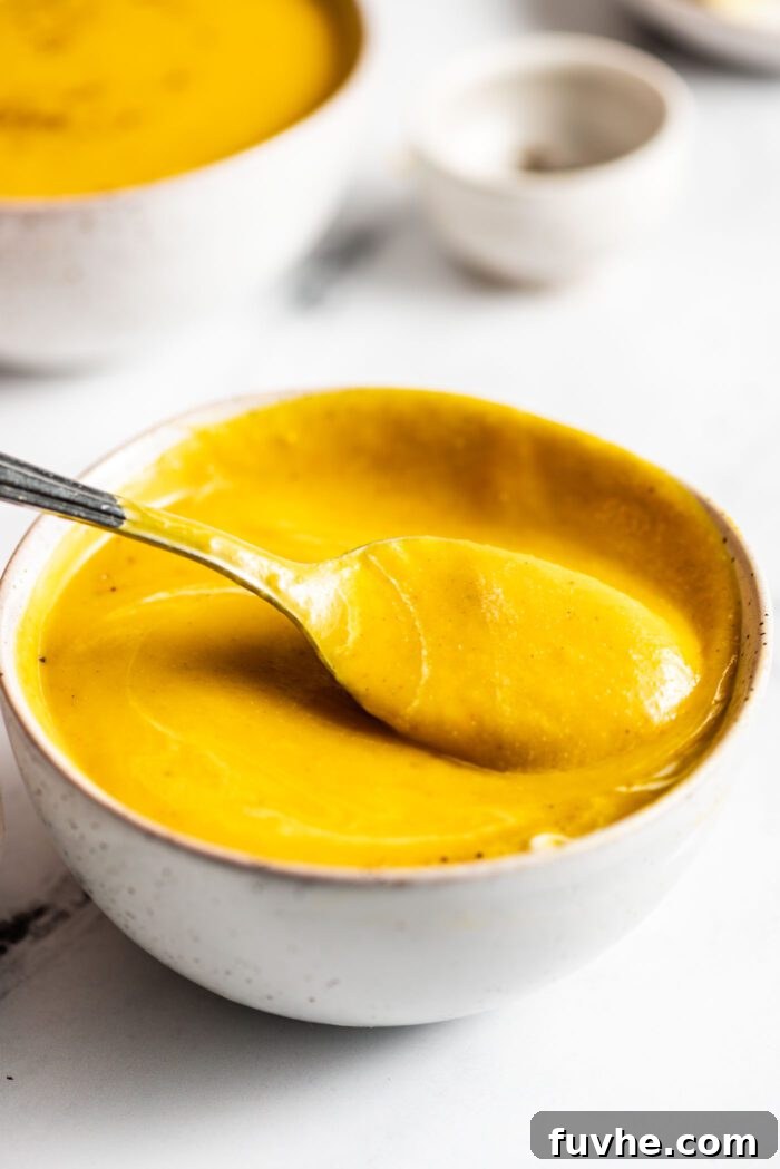 Silken Kabocha Squash Soup 11 A spoon lifts a generous portion of rich, creamy kabocha squash soup from a bowl, highlighting its velvety texture and vibrant color.