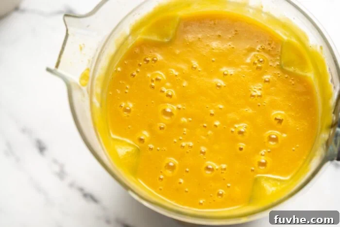 Silken Kabocha Squash Soup 9 The creamy, vibrant orange squash soup is being blended to perfection in a high-speed blender container.