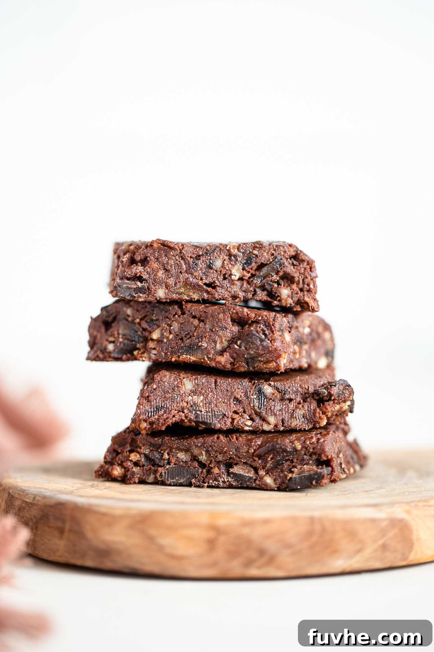A stack of 4 rich, dark brown raw vegan brownies on a rustic cutting board, sprinkled with cocoa powder.