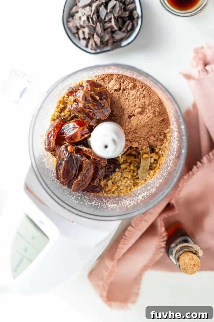 Cocoa powder, dates, and processed walnuts combined in a food processor bowl, ready to be blended into dough.