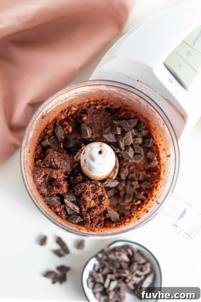 Thick chocolate brownie dough in a food processor with dark chocolate chunks mixed in.
