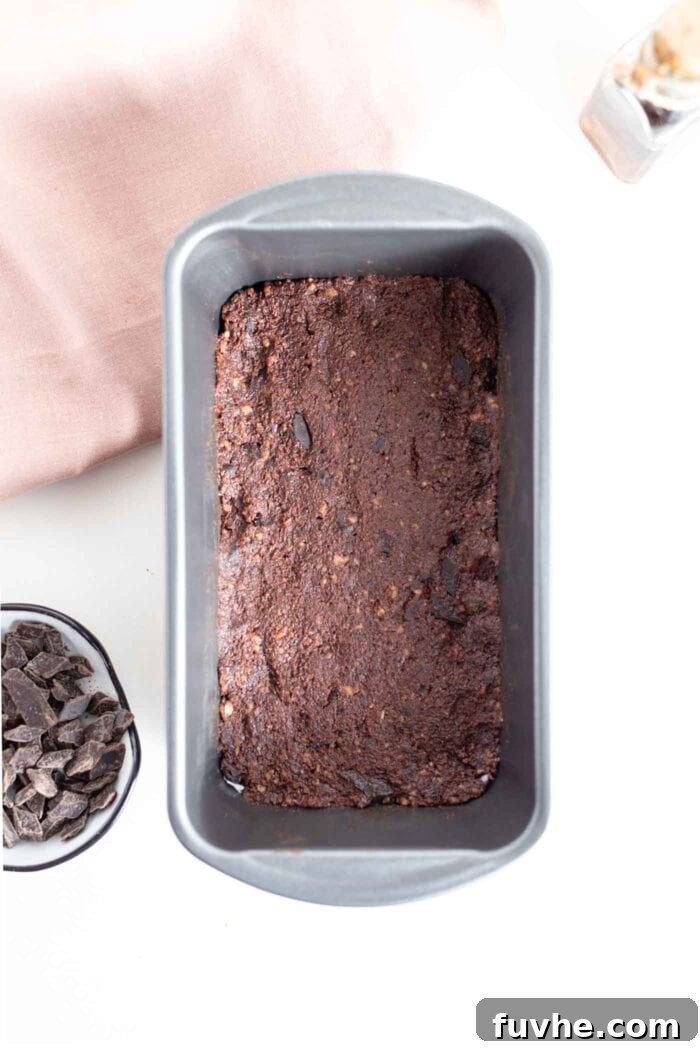 Raw vegan brownie mixture firmly pressed into a parchment-lined loaf pan.