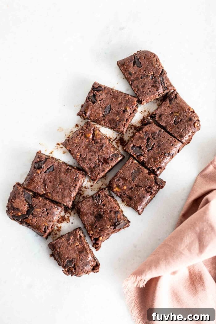 An overhead view of a large slab of chilled raw vegan brownies, perfectly sliced into 8 rectangular pieces on a wooden cutting board.